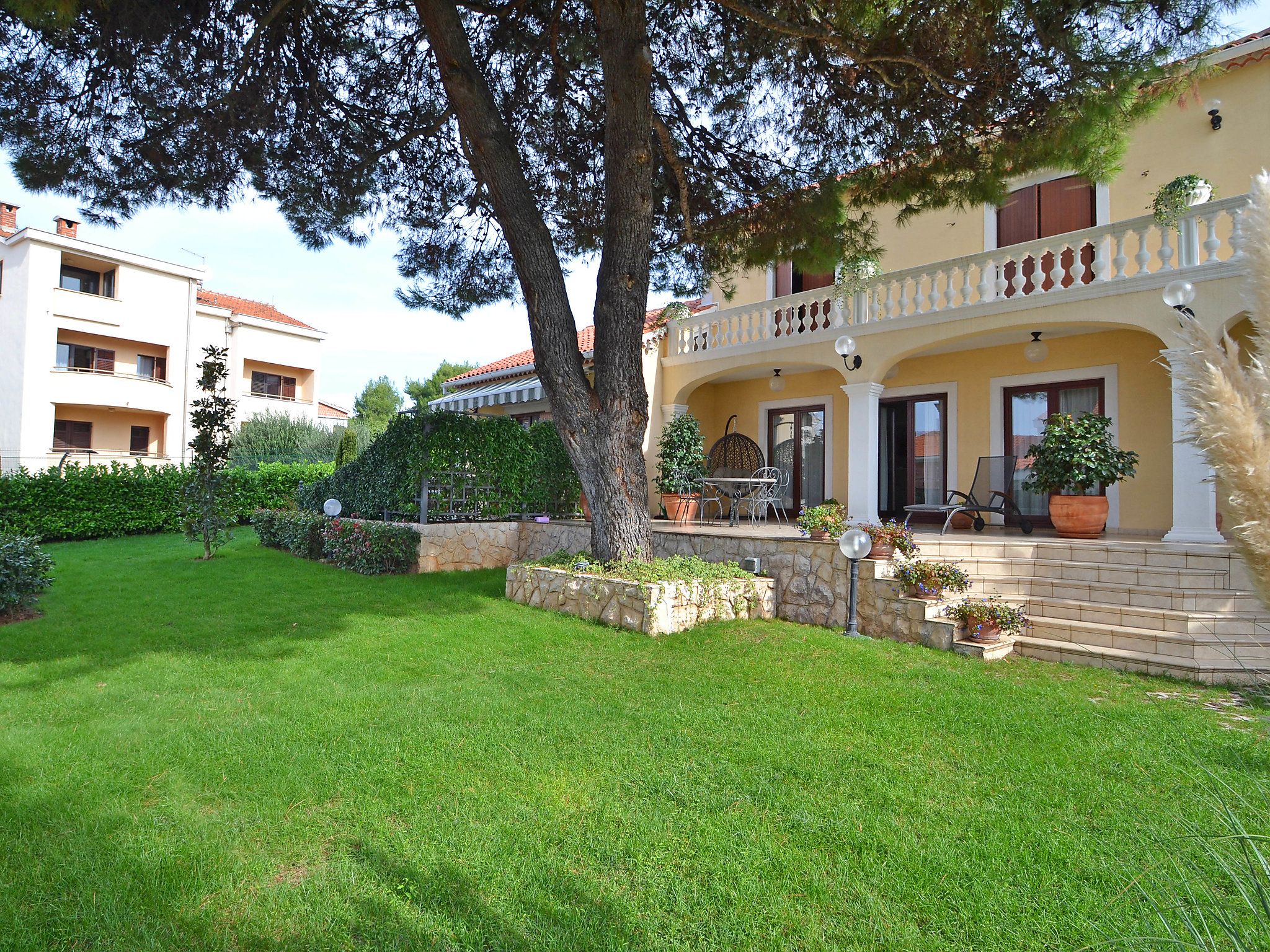 A residential building with a balcony, a stone pathway, and a well-maintained lawn.