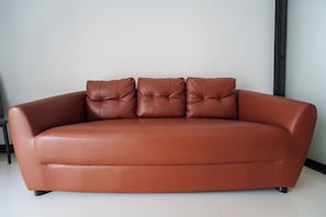 A brown leather sofa with a tufted backrest and three cushions, positioned against a plain wall with a black floor lamp to the right. - Elyana -Serene 3BR Pool Villa Retreat (Tambon Rawai)