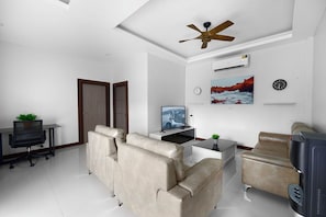 A modern living room with a sofa, a television, a desk with a computer, and a ceiling fan. - Elyana -Serene 3BR Pool Villa Retreat (Tambon Rawai)
