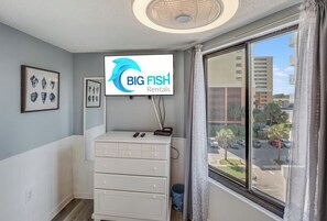 A hotel room with a large window, a flat-screen TV mounted above a white dresser, and framed artwork on the wall. - Breathtaking Ocean Views Your Beachside Getaway (Myrtle Beach)
