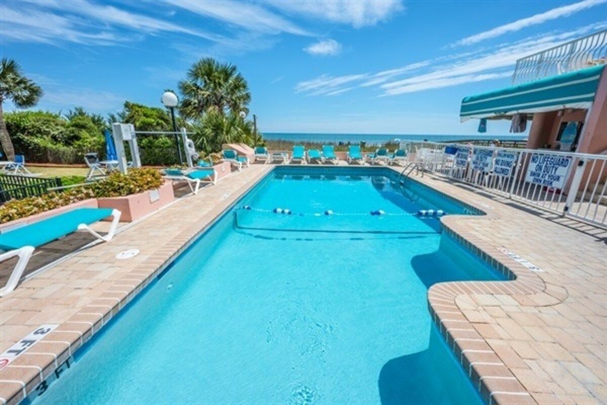 A swimming pool with a lifeguard station, lounge chairs, and a view of the ocean.