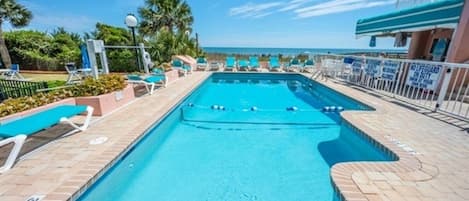 A swimming pool with a lifeguard station, lounge chairs, and a view of the ocean.