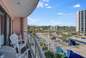 A balcony with white chairs, a view of a parking lot, and buildings in the distance. - Breathtaking Ocean Views Your Beachside Getaway (Myrtle Beach)