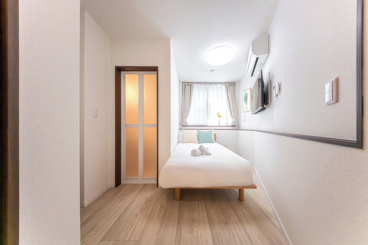 Ein modernes Hotelzimmer mit einem Bett, einem Fenster mit Vorhängen, einem am Wand montierten Flachbildfernseher und einem Holzboden.