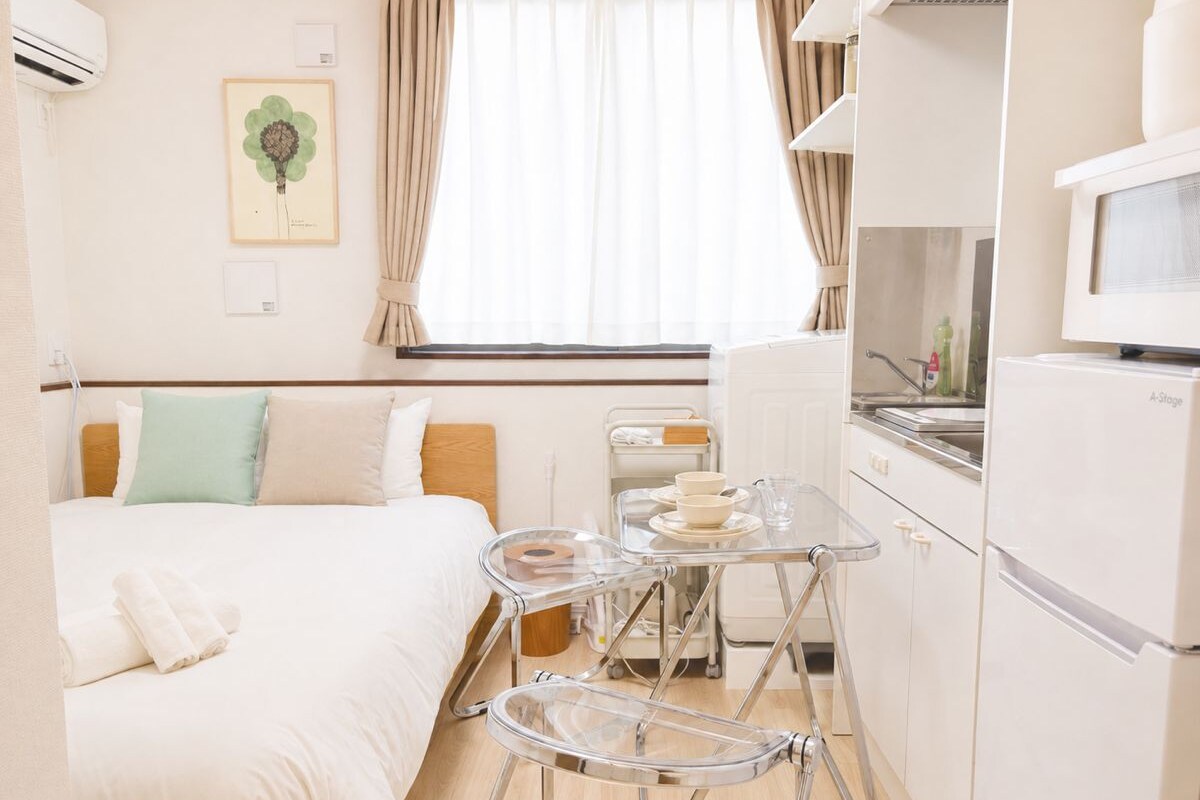 Ein Hotelzimmer mit einem Bett, einem kleinen Tisch mit Tablett, einem Kühlschrank und einem Fenster mit Vorhängen.