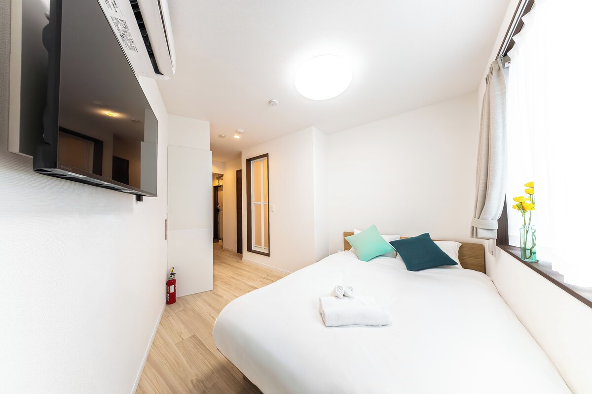 Ein Hotelzimmer mit Bett, Fenster mit Vorhängen, Nachttisch und Spiegel.