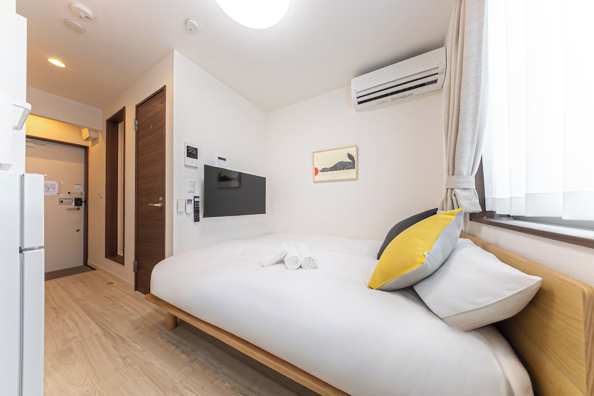 Ein Hotelzimmer mit Bett, Fernseher, Klimaanlage, einer Tür und einem Fenster mit Vorhängen.