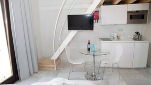 A modern hotel room with a bed, a glass table with two chairs, a kitchen area with a microwave, and a TV mounted on the wall. - Malaga City Breaks (Málaga)