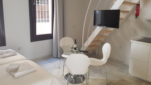 A modern hotel room with a bed, a dining table with chairs, a TV mounted on a wall, and a staircase. - Malaga City Breaks (Málaga)