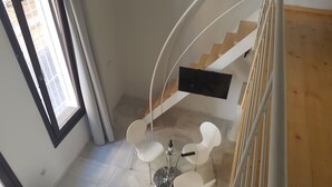 A modern interior with a spiral staircase, a flat-screen TV, and a dining area with white chairs and a table. - Malaga City Breaks (Málaga)