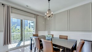 Ein Esszimmer mit einem großen Tisch, sechs Stühlen, einer Kristallleuchter und einer Schiebeglastür, die auf einen Balkon führt.