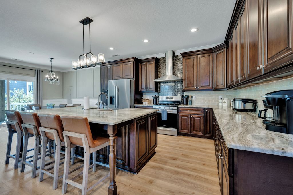 A modern kitchen with dark wood cabinets, a large island with bar stools, stainless steel appliances, and a chandelier.
