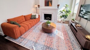 A living room with a sofa, a fireplace, a coffee table, and a television. - Charming Historic 2BR Townhouse 10-Min PATH Ride to NYC (Jersey City)