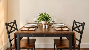 A dining table with four chairs, a potted plant, and a set of plates and wine glasses. - Charming Historic 2BR Townhouse 10-Min PATH Ride to NYC (Jersey City)