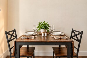 Une table à manger avec quatre chaises, une plante en pot et un ensemble d’assiettes et de verres à vin.