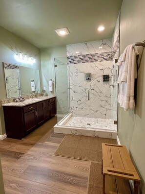 Un baño moderno con ducha de vidrio, tocador de mármol y banco de madera.