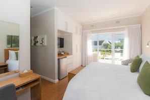 Ett modernt hotellrum med en stor säng, ett skrivbord, ett litet pentry och en balkong med utsikt över omgivningen.