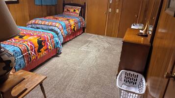 A bedroom with two beds, a wooden headboard, a small wooden table, a laundry basket, and a wooden cabinet.