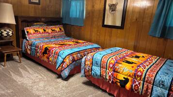 A room with two beds, a wooden headboard, a nightstand, a lamp, and a framed picture on the wall.