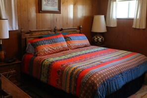 A wooden bed with colorful bedding and a nightstand with a lamp.