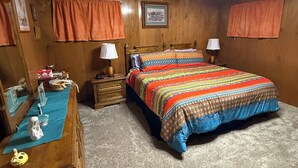 Ein Schlafzimmer mit einem hölzernen Kopfende, einem Bett mit farbenfroher Decke, zwei Nachttischen mit Lampen, einem Schminktisch und einem Spiegel.