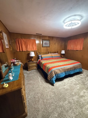 Una camera da letto con una testiera in legno, un letto con copriletto colorato, due comodini con lampade, una cassettiera e uno specchio.