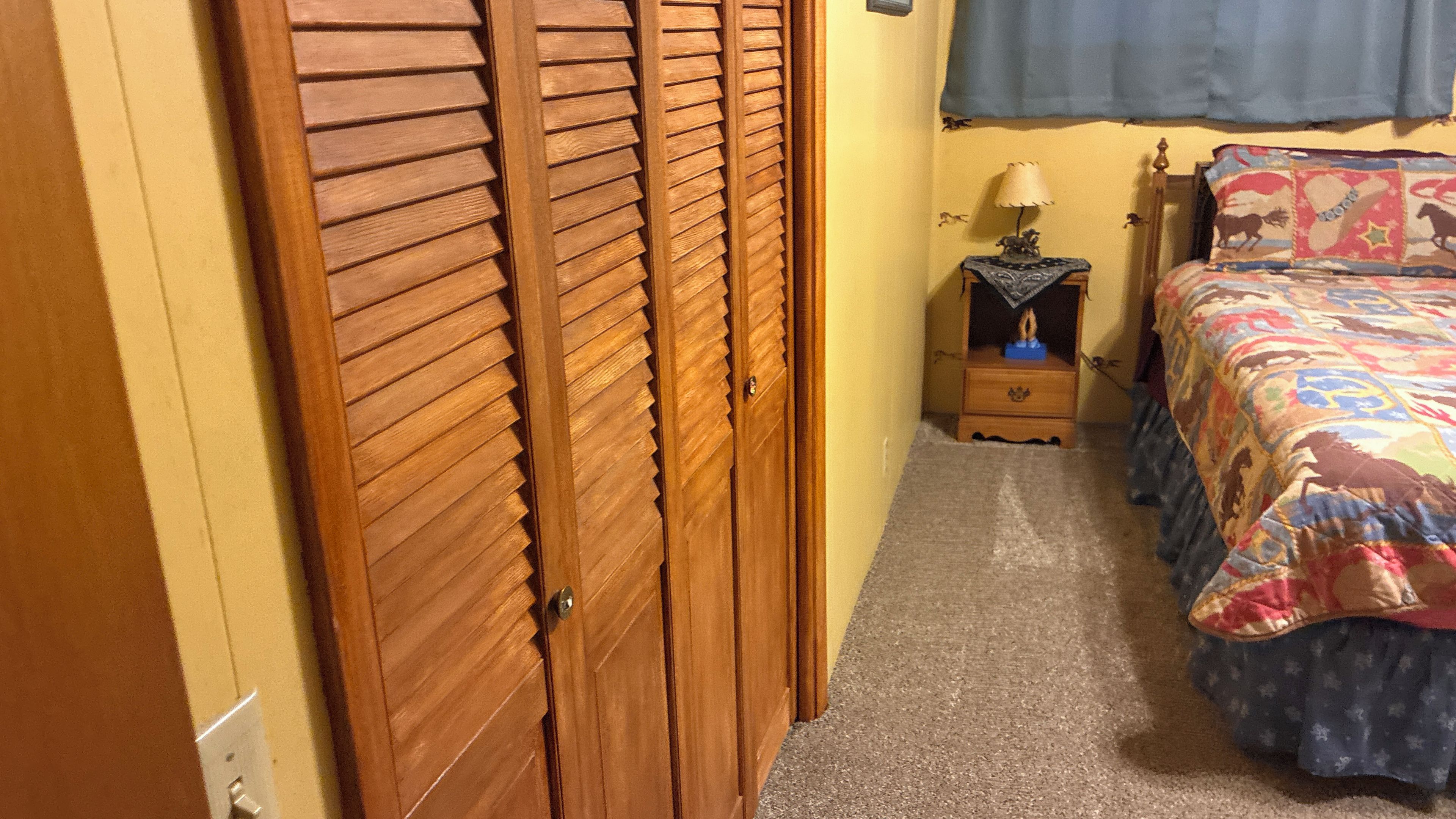 A bedroom with a wooden wardrobe, a bedside table with a lamp, and a bed with a colorful blanket.