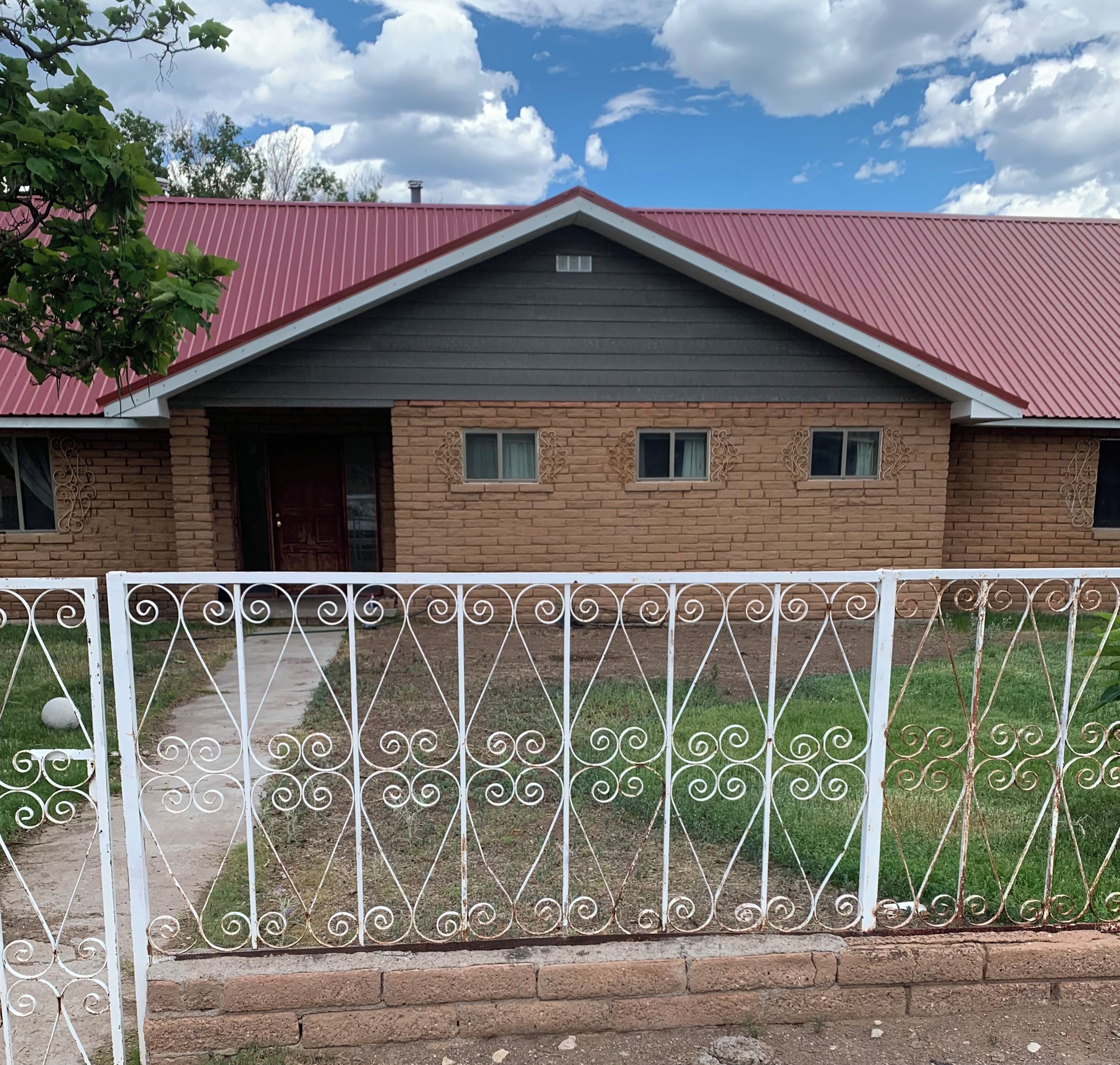 Uma casa de dois andares com telhado vermelho, paredes de tijolo e cerca de metal ao primeiro plano.