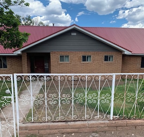 A two-story house with a red roof, brick walls, and a metal fence in the foreground.