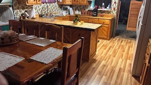 A wooden dining table with placemats, a kitchen area with wooden cabinets, and a wooden floor.