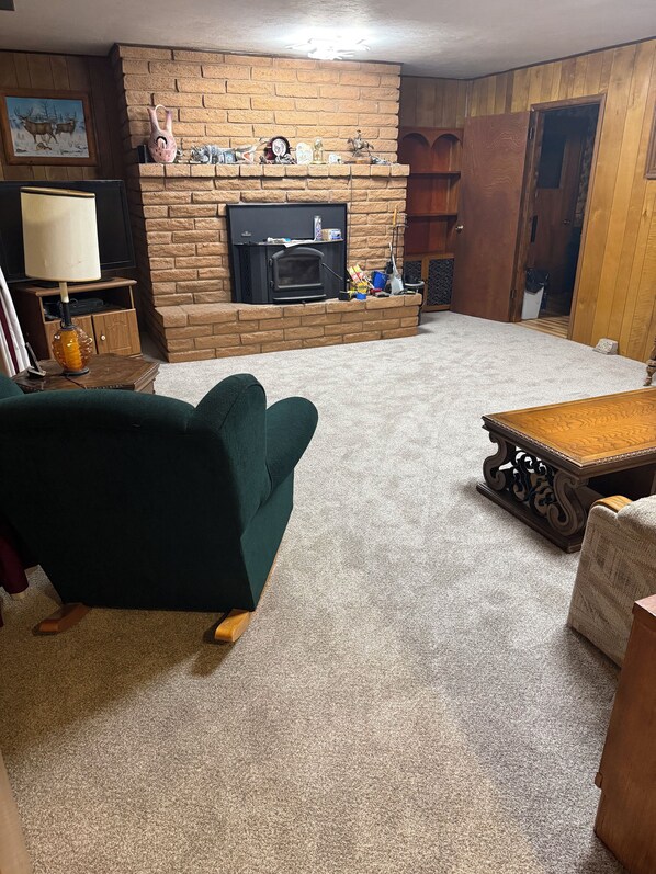A living room with a brick fireplace, a green armchair, a wooden coffee table, and a television.