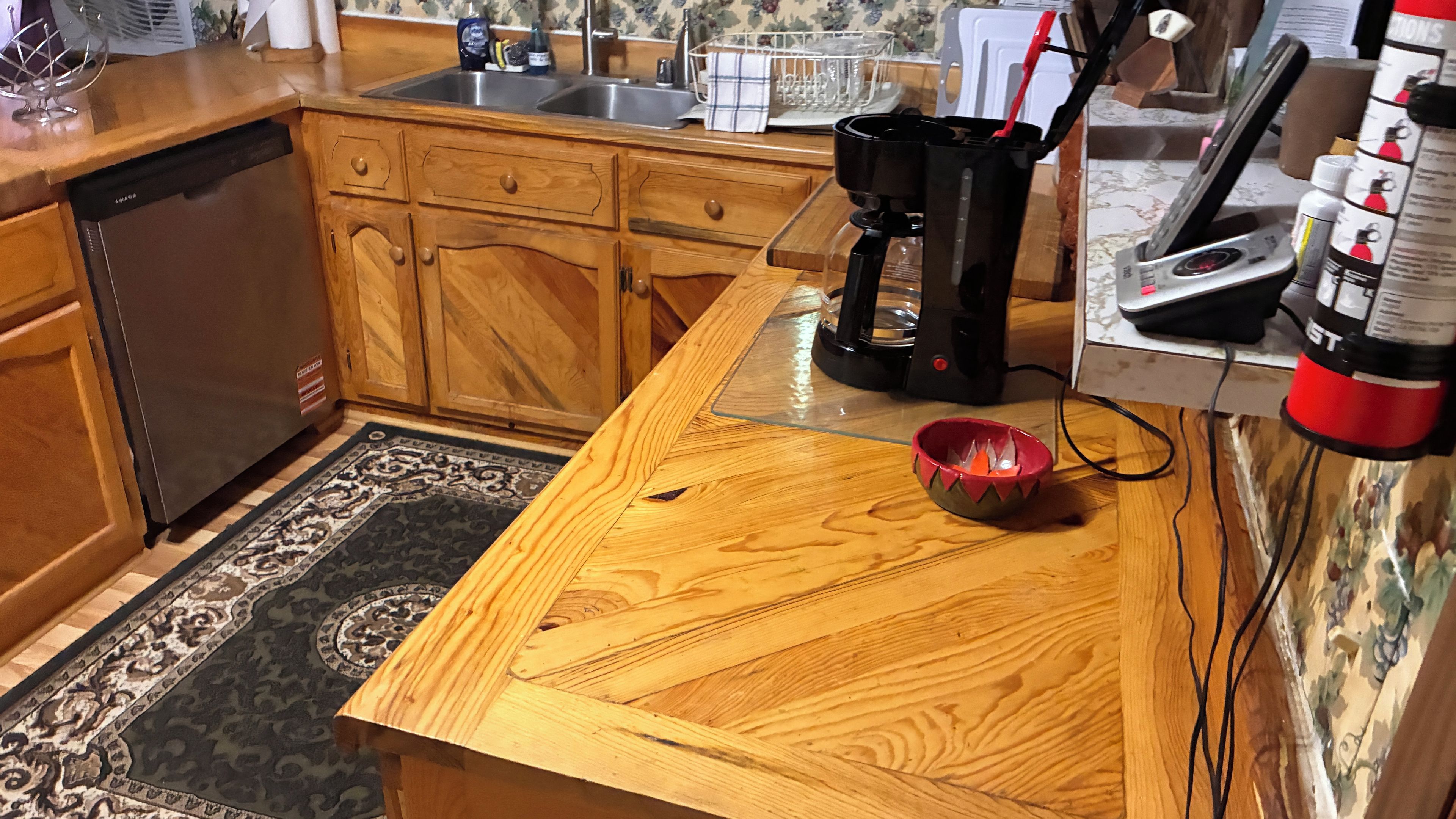 A kitchen with wooden cabinets, a dishwasher, a coffee maker, and a red bowl on the counter.