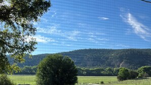 Ein runder Metalltisch mit aufwendigen Verzierungen, ein Metallstuhl und im Hintergrund ein Blick auf ein grünes Feld mit Bäumen und Hügeln.