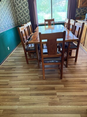 A dining area with a wooden table and chairs, a patterned wall, and a window with curtains.
