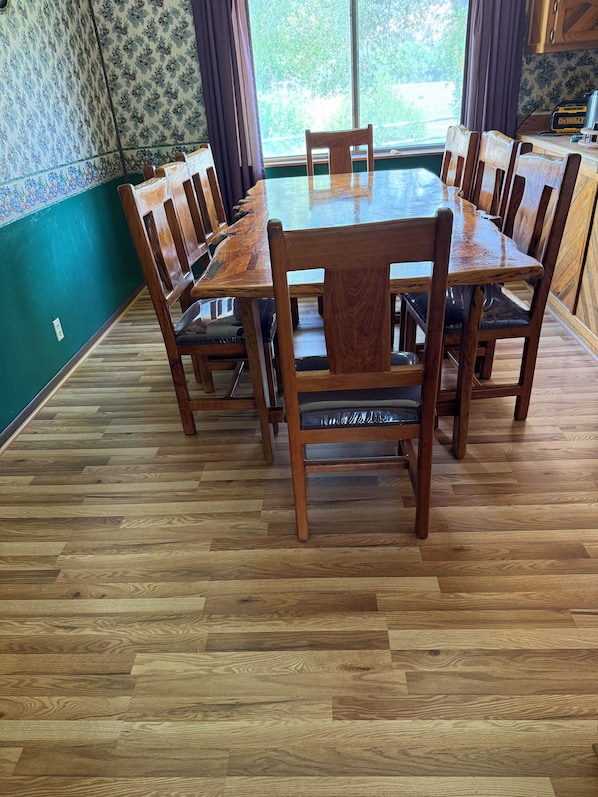 Un'area pranzo con tavolo e sedie in legno, parete decorata e finestra con tende.