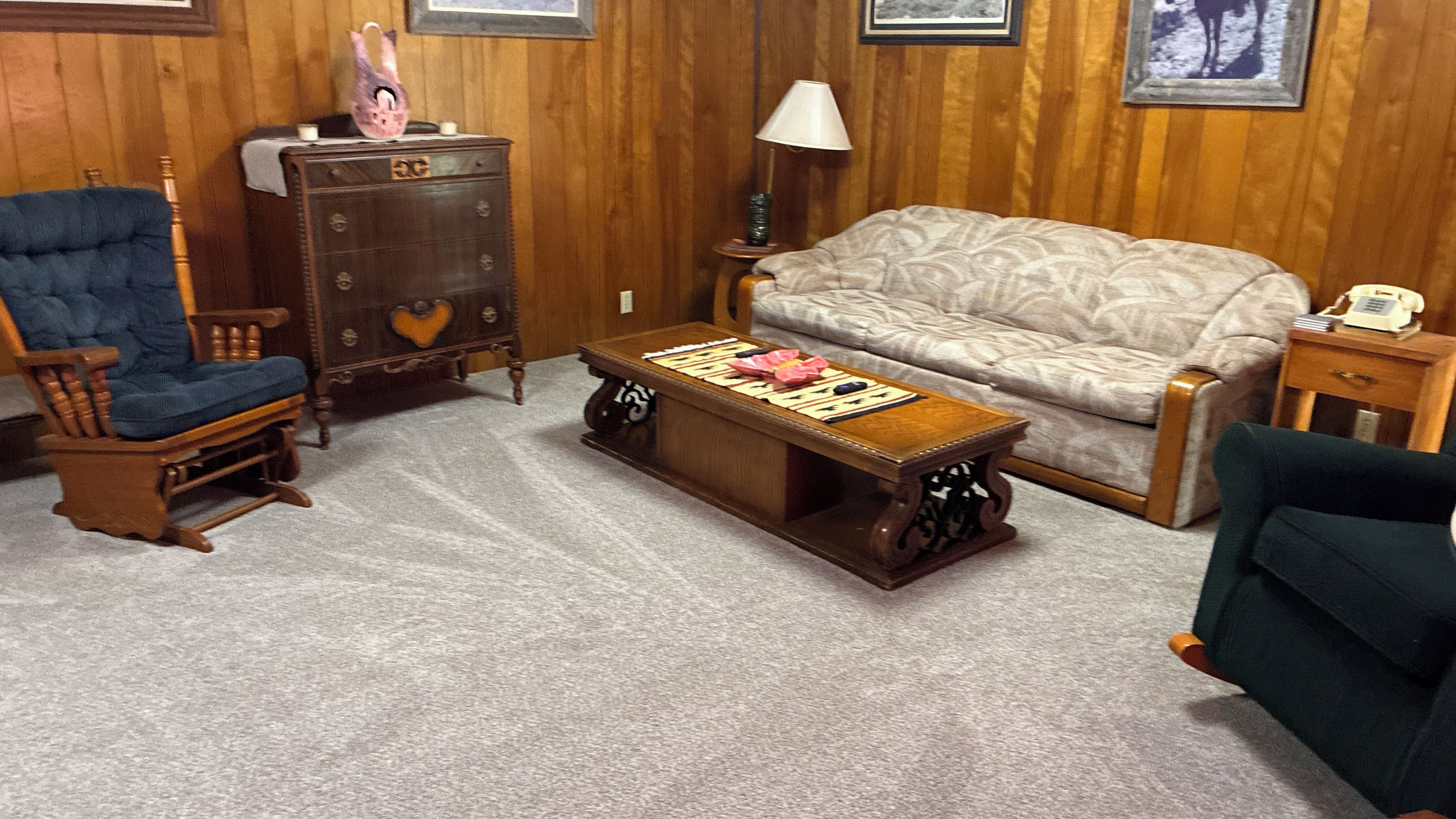 A room with a rocking chair, a sofa, a wooden coffee table, a dresser, and a lamp.