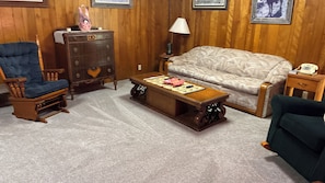 A room with a rocking chair, a sofa, a wooden coffee table, a dresser, and a lamp.