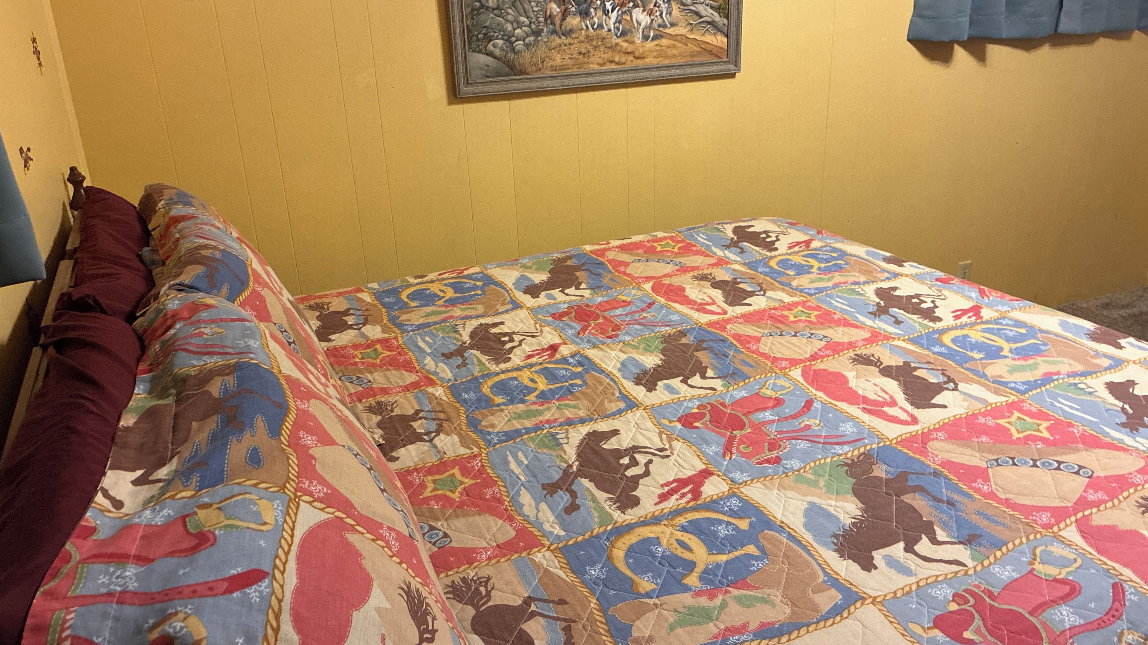 A bed with a colorful quilt featuring animal prints, a wooden headboard, and a painting on the wall.