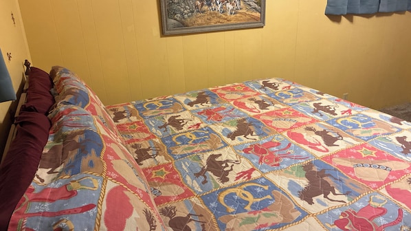 A bed with a colorful quilt featuring animal prints, a wooden headboard, and a painting on the wall.