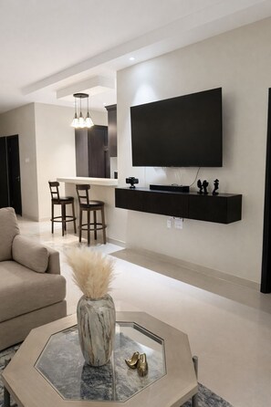 A modern living room with a flat-screen TV mounted on the wall, a sofa, a coffee table with decorative items, and a dining area with chairs and a kitchen island. - Spacious 3-bedroom house in wonderful Ocho Rios with AC and infinity pool. (Ocho Rios)