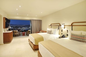 Ein Hotelzimmer mit zwei Betten, einem Schreibtisch und Blick auf eine Stadtlandschaft.