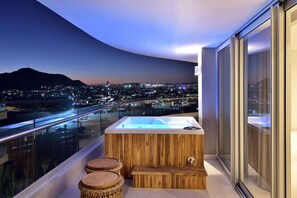 Ein Balkon mit Whirlpool, Holzschemeln und Blick auf die Stadt im Abenddämmerung.