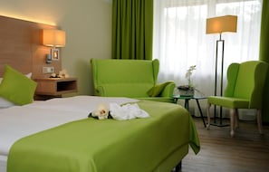 A hotel room with a bed, two green armchairs, a small table with a plant, and a lamp. - Parkhotel-forsthaus Dresden (Tharandt)