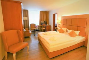 A hotel room with a large bed, a chair, a desk with a TV, and a window with curtains. - Parkhotel-forsthaus Dresden (Tharandt)