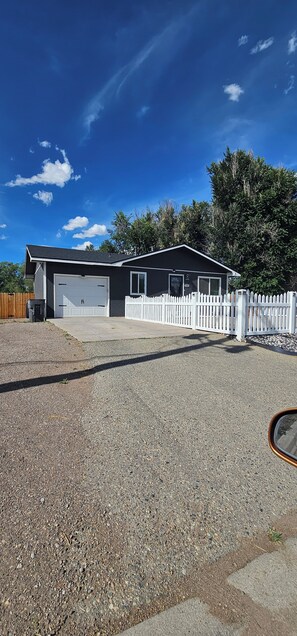 A single-story building with a garage, a white picket fence, and a gravel driveway.