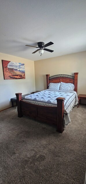 Ein Schlafzimmer mit einem hölzernen Bett, einem Deckenventilator, einem Nachttisch und einem an der Wand befestigten Gemälde.