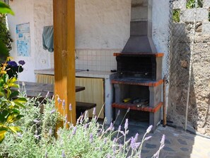 Un área de cocina al aire libre con un horno de ladrillo, una mesa de madera y un muro de piedra.
