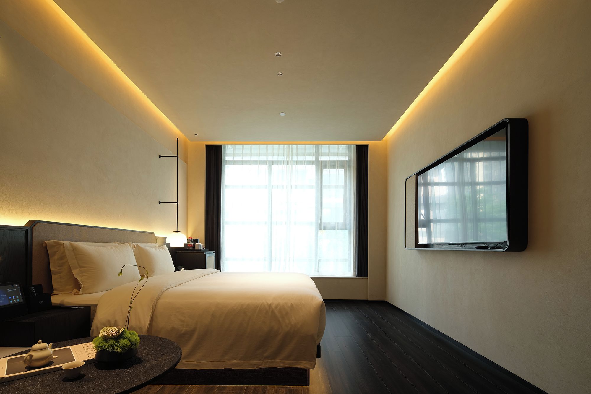 Una habitación de hotel moderna con una cama grande, una mesita de noche y un televisor de pantalla plana montado en la pared.