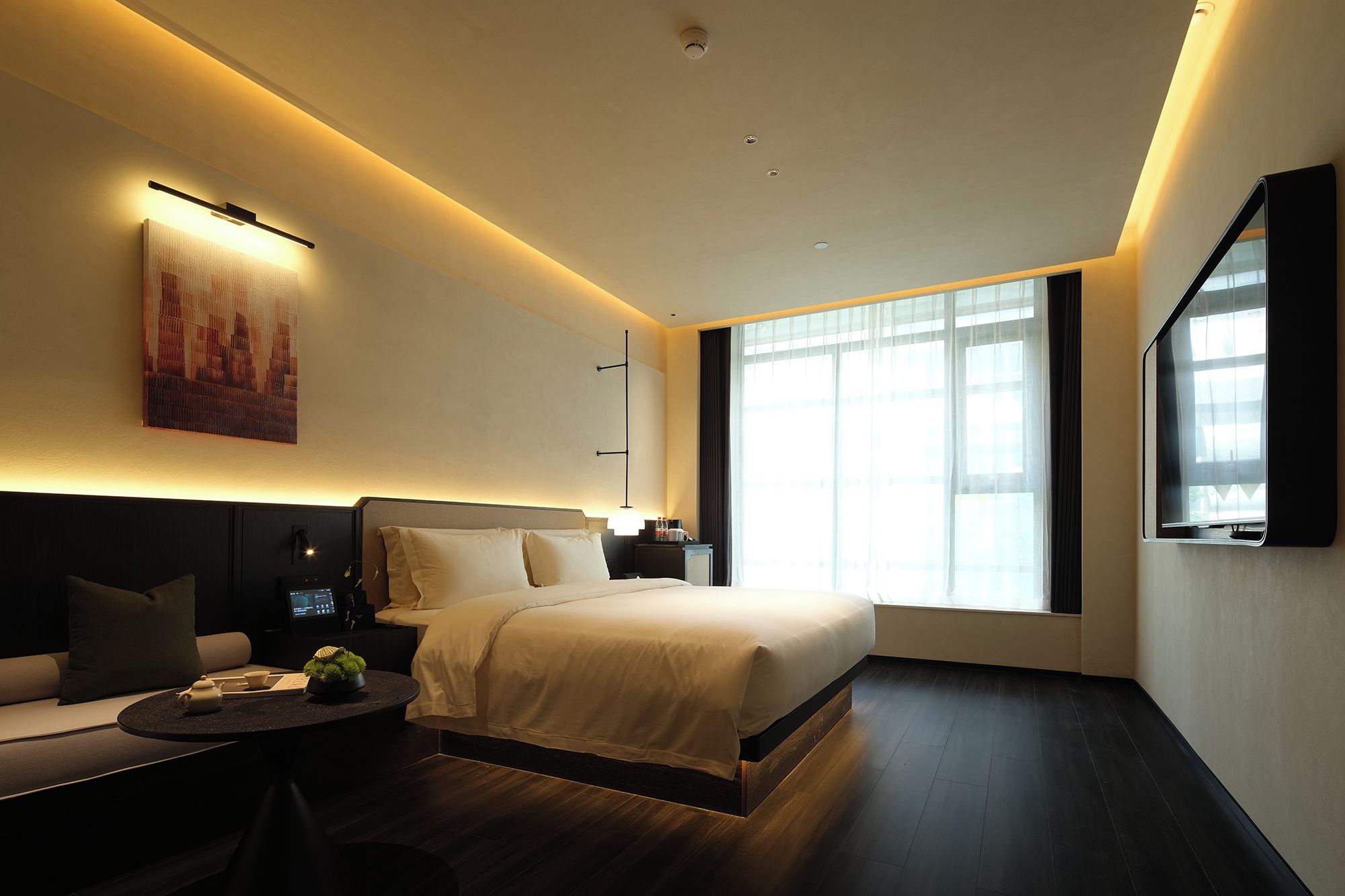 Una habitación de hotel moderna con una cama grande, una zona de estar con una mesa y un ventanal que proporciona luz natural.