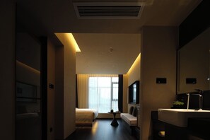 Habitación de hotel con cama, sofá, una mesita, televisión y baño con lavamanos y espejo.